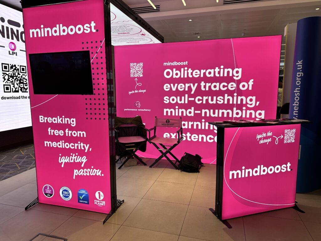 Absorbent, vibrant pink exhibition booth with bold white text promoting mindboost's focus on obliterating soul-crushing, mind-numbing existence and igniting passion through innovative performance consultancy.