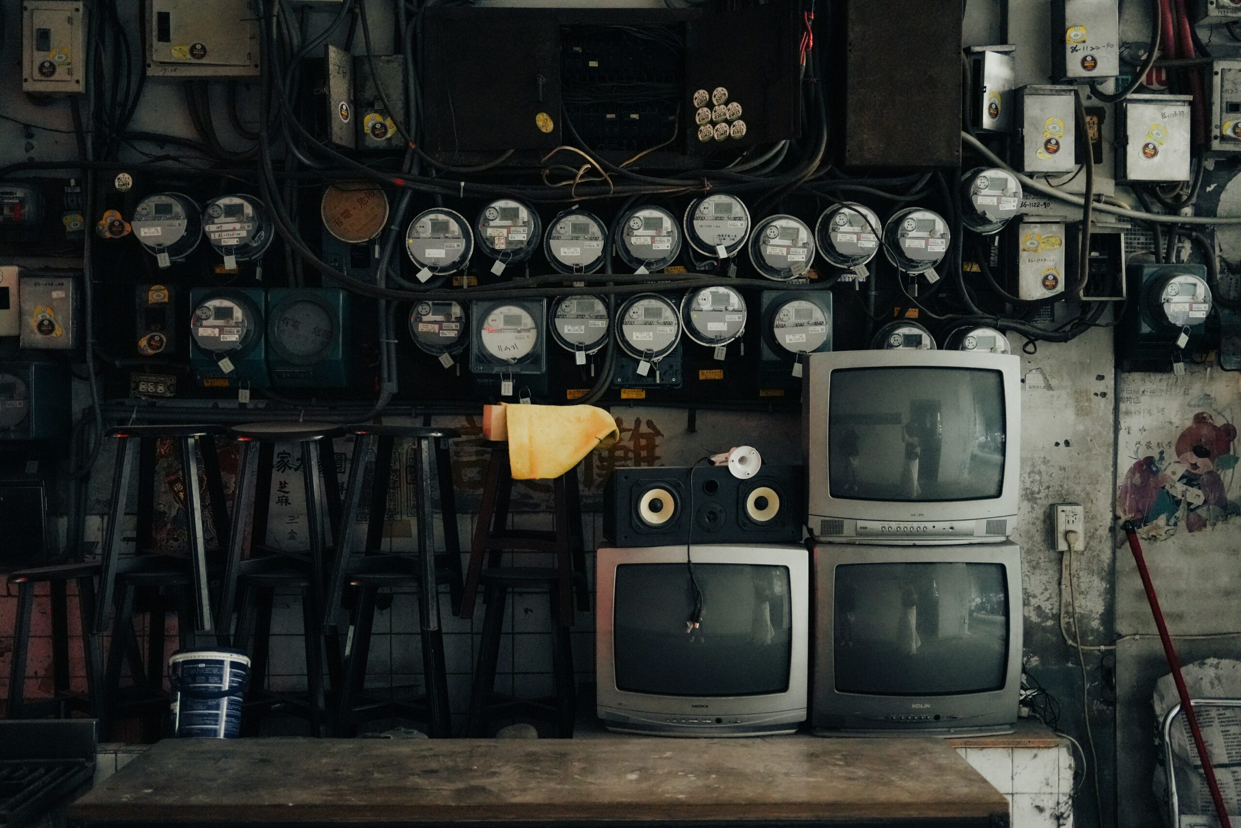 Electric meters and old televisions in a cluttered utility room, representing outdated technology and energy consumption; grungy, vintage, and industrial setting.