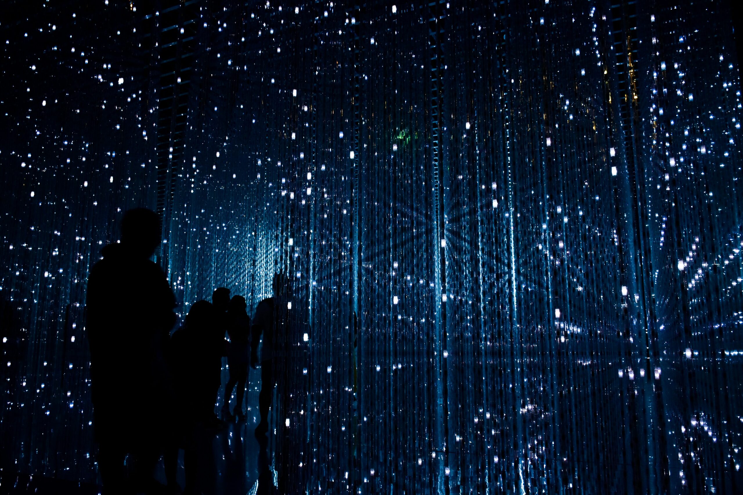 Illuminated art installation with hanging LED lights creating a starry effects, visitors exploring a captivating digital exhibition. Perfect for inspiring creativity and innovation in learning environments.