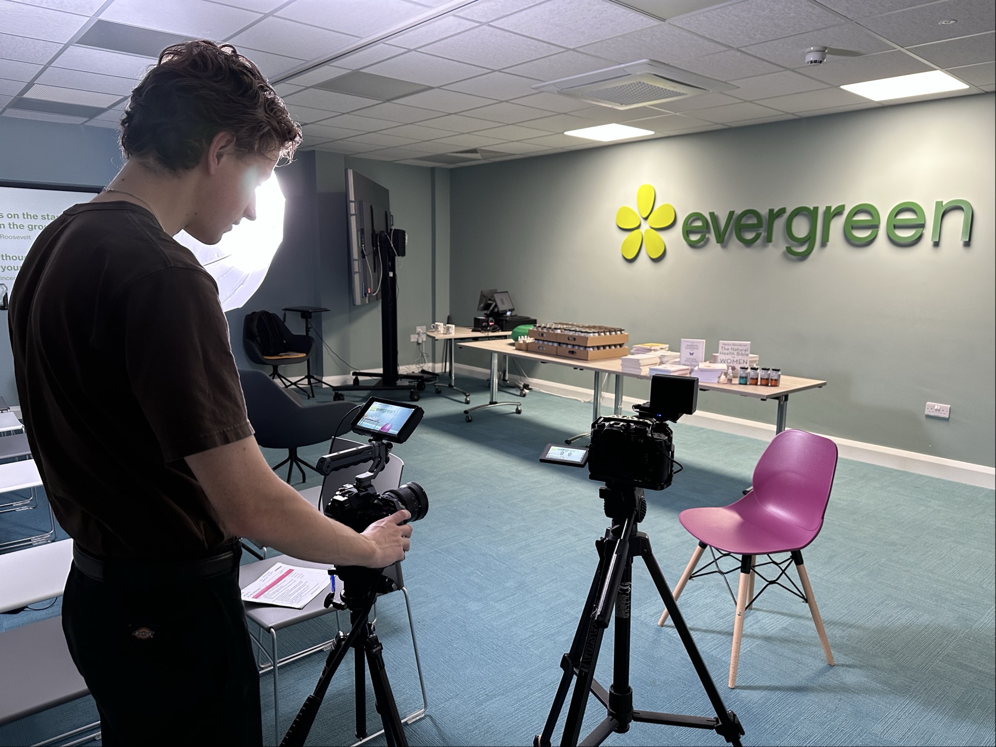 Camera setup for corporate video production at Evergreen office, modern studio with professional filming equipment, Green background, and marketing materials, ideal for educational or promotional content.
