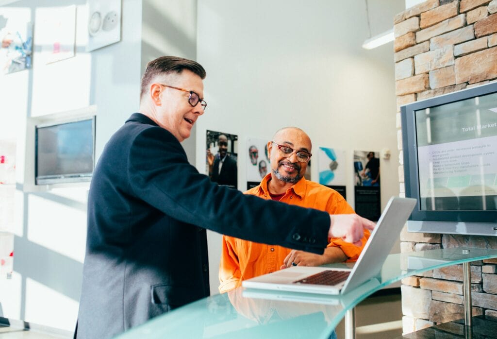 linkedin-sales-solutions-YDVdprpgHv4-unsplash | mindboost. Innovative collaboration in a modern office environment with two professionals discussing on a laptop, representing teamwork and business growth.