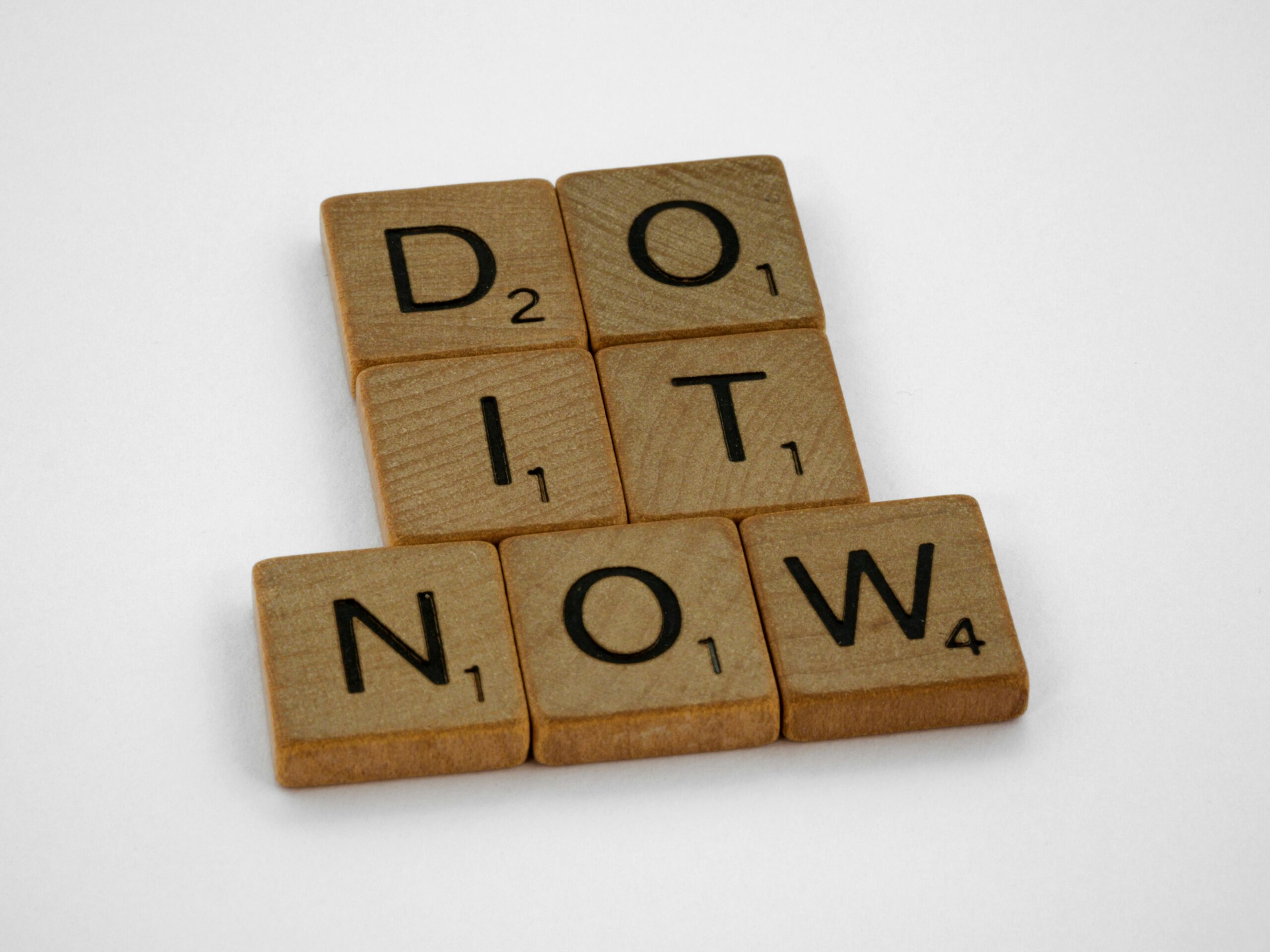 Wooden Scrabble tiles spelling "DO IT NOW" symbolising urgency and action in learning and development ROI strategies.