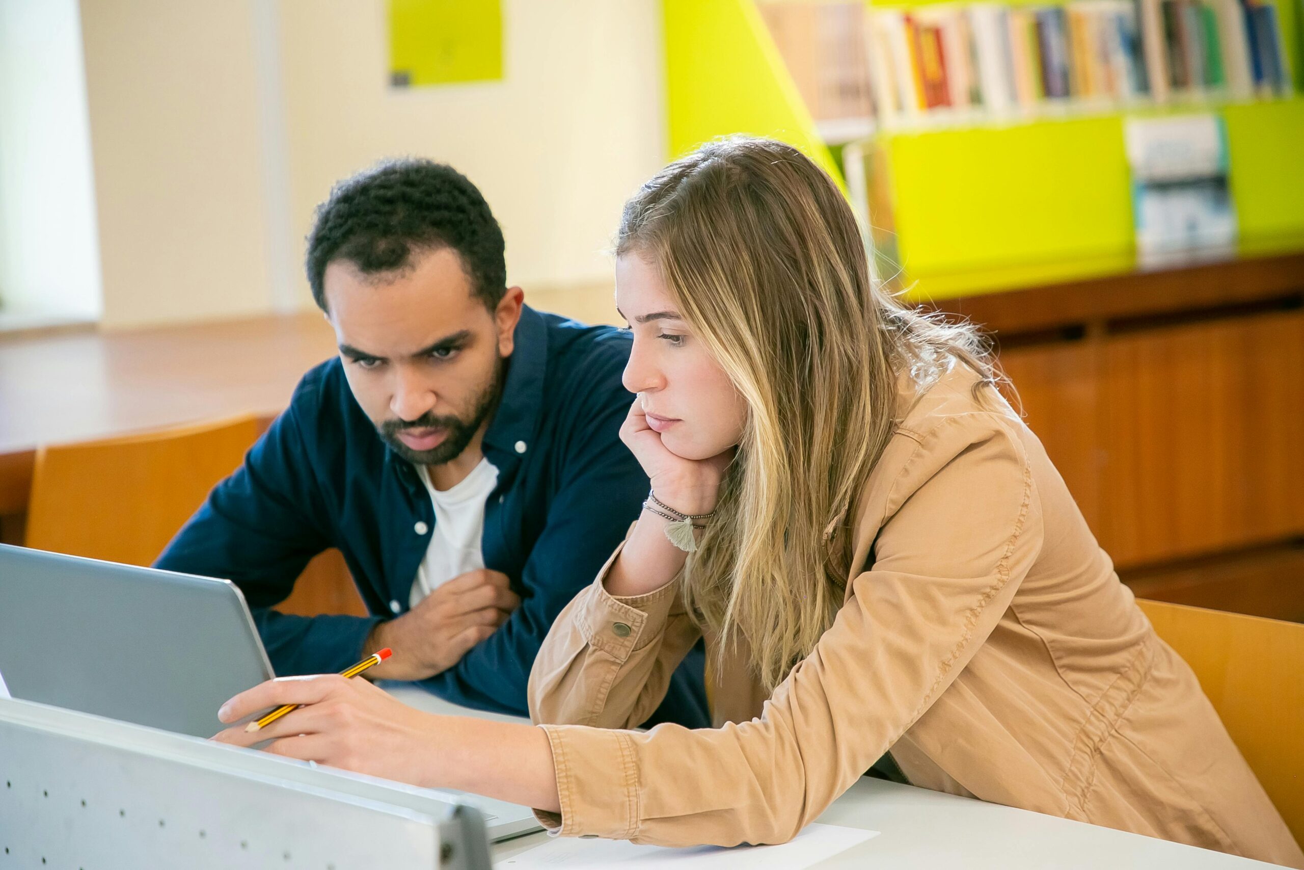 Two students collaborating on a tablet in a library, exploring AI tools for learning and development, highlighting challenges and solutions in integrating AI in corporate training.
